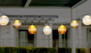 Lichterkette mit kugelförmigen, geriffelten Lampenschirmen in warmen Farben, aufgehängt in einem Außenbereich, seitliche Perspektive
