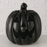 Schwarzer Halloween-Kürbis (Jack-o’-Lantern) mit geschnitztem Gesicht, frontal aus leicht erhöhter Perspektive vor weißer Ziegelwand