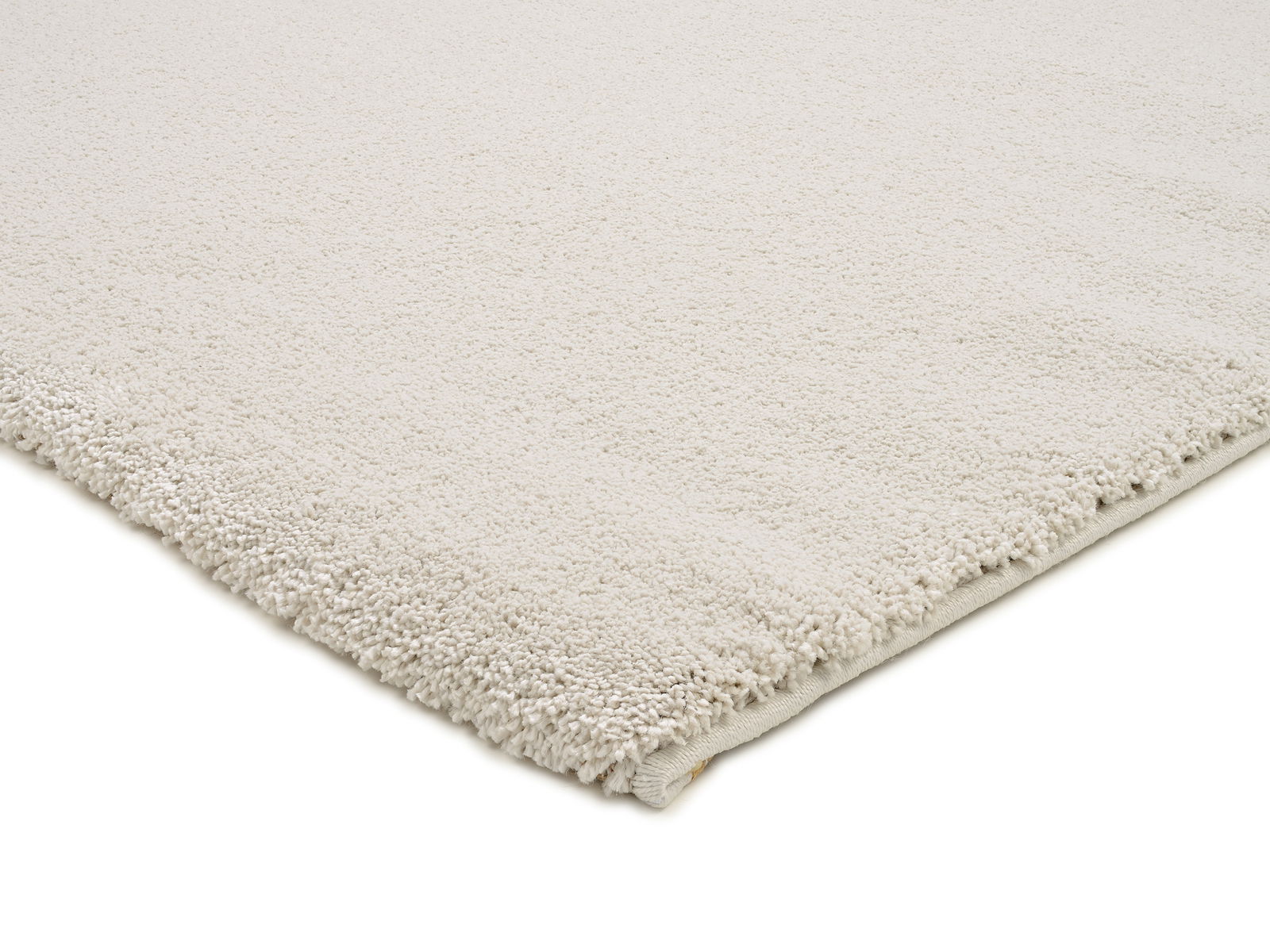 Nahaufnahme eines cremefarbenen Uni-Teppichs mit weicher, flauschiger Textur, von der Seite fotografiert.