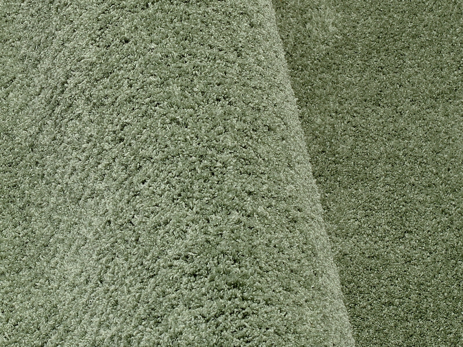Nahaufnahme eines weichen, grünen Teppichs mit flauschiger Textur, perspektivisch von der Seite aufgenommen.
