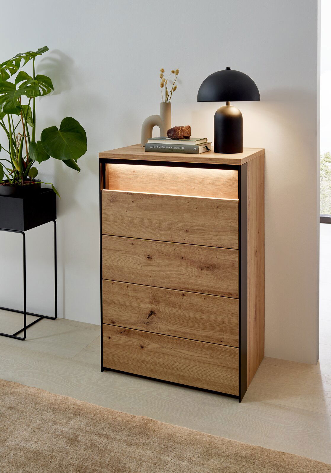 Hochkommode aus Holz mit vier Schubladen, dekoriert mit einer Lampe und Büchern, seitliche Perspektive