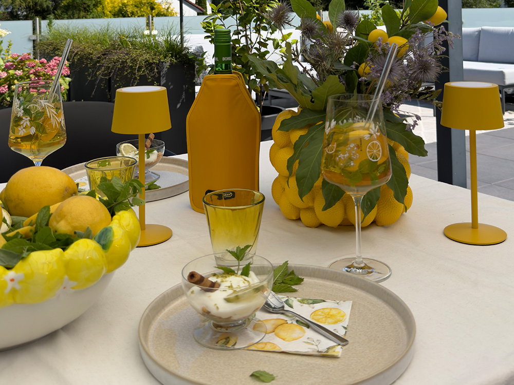 Terrassentisch mit Zitronendeko, Getränken und gelben Tischleuchten.