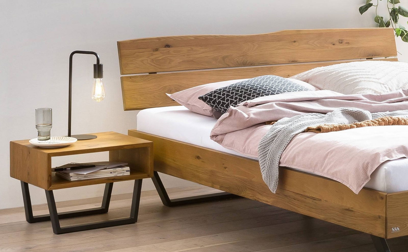 Holzbettgestell mit modernem Design, seitliche Perspektive, neben einem Nachttisch mit Lampe und Glas.