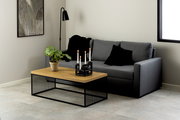 Moderner Couchtisch mit Holzplatte und schwarzem Metallgestell, dekoriert mit einer Pflanze und Kerzenhalter, seitliche Perspektive.