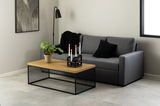 Moderner Couchtisch mit Holzplatte und schwarzem Metallgestell, dekoriert mit einer Pflanze und Kerzenhalter, seitliche Perspektive.