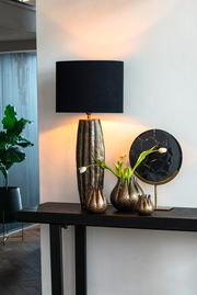 Eleganter, ovaler Lampenschirm in Schwarz auf einem dekorativen Tisch mit Vasen und Pflanzen, seitliche Perspektive.