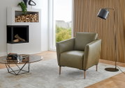 Moderner grüner Sessel Valnatura Polstermöbel PERLA in einem stilvollen Wohnzimmer mit Holzvertäfelung und Stehlampe, seitliche Perspektive.