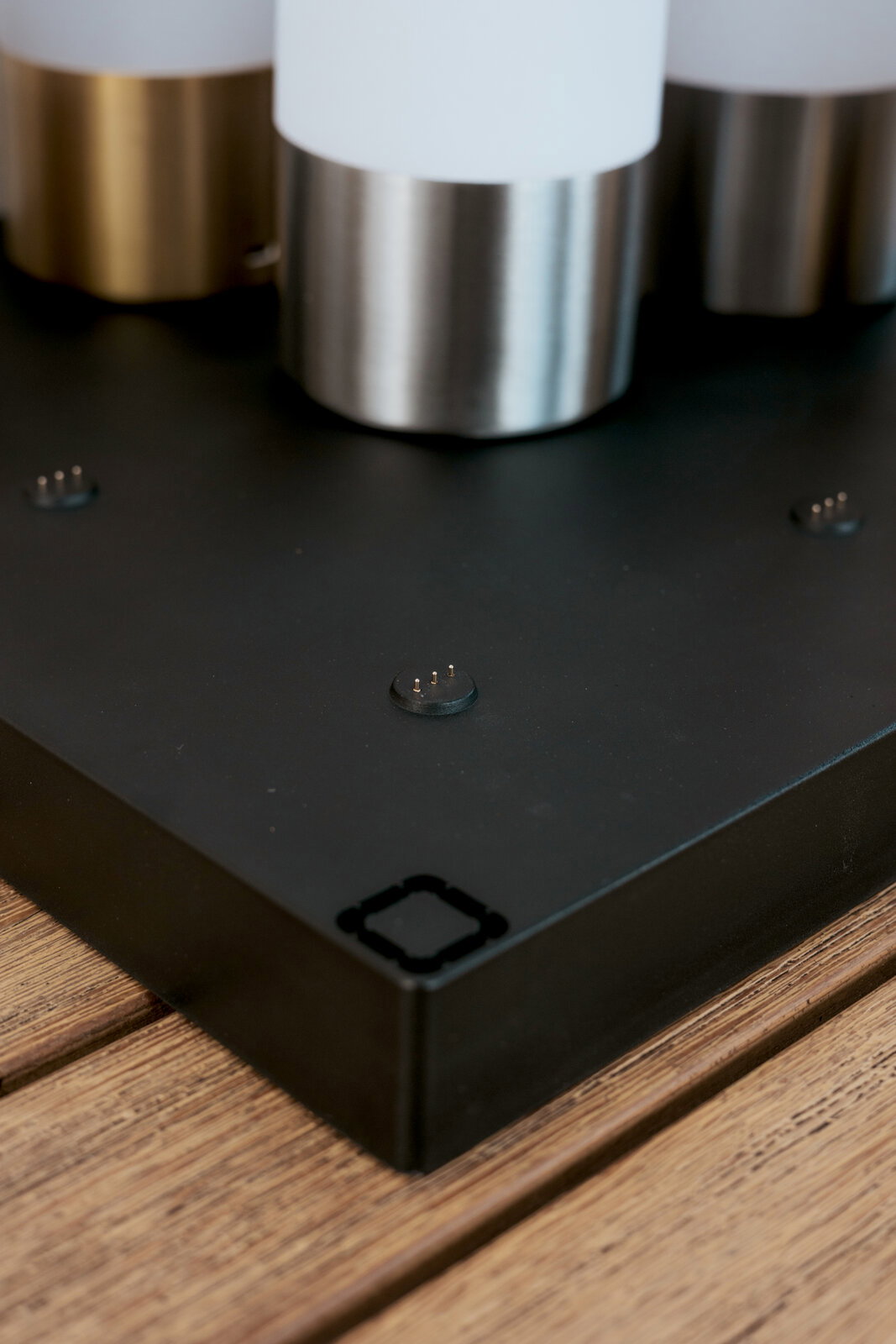 Close-up vanuit een licht verhoogd perspectief van een zwarte metalen voet met contactpinnen en drie cilindervormige metalen bevestigingen op een houten oppervlak.