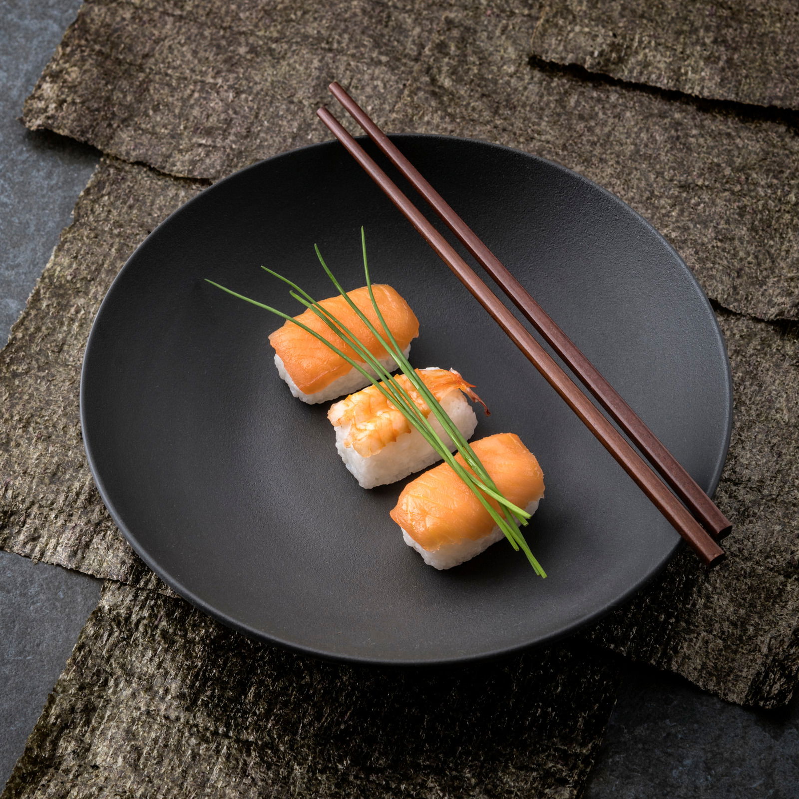 Schwarze Schale mit Sushi und Essstäbchen, von oben fotografiert