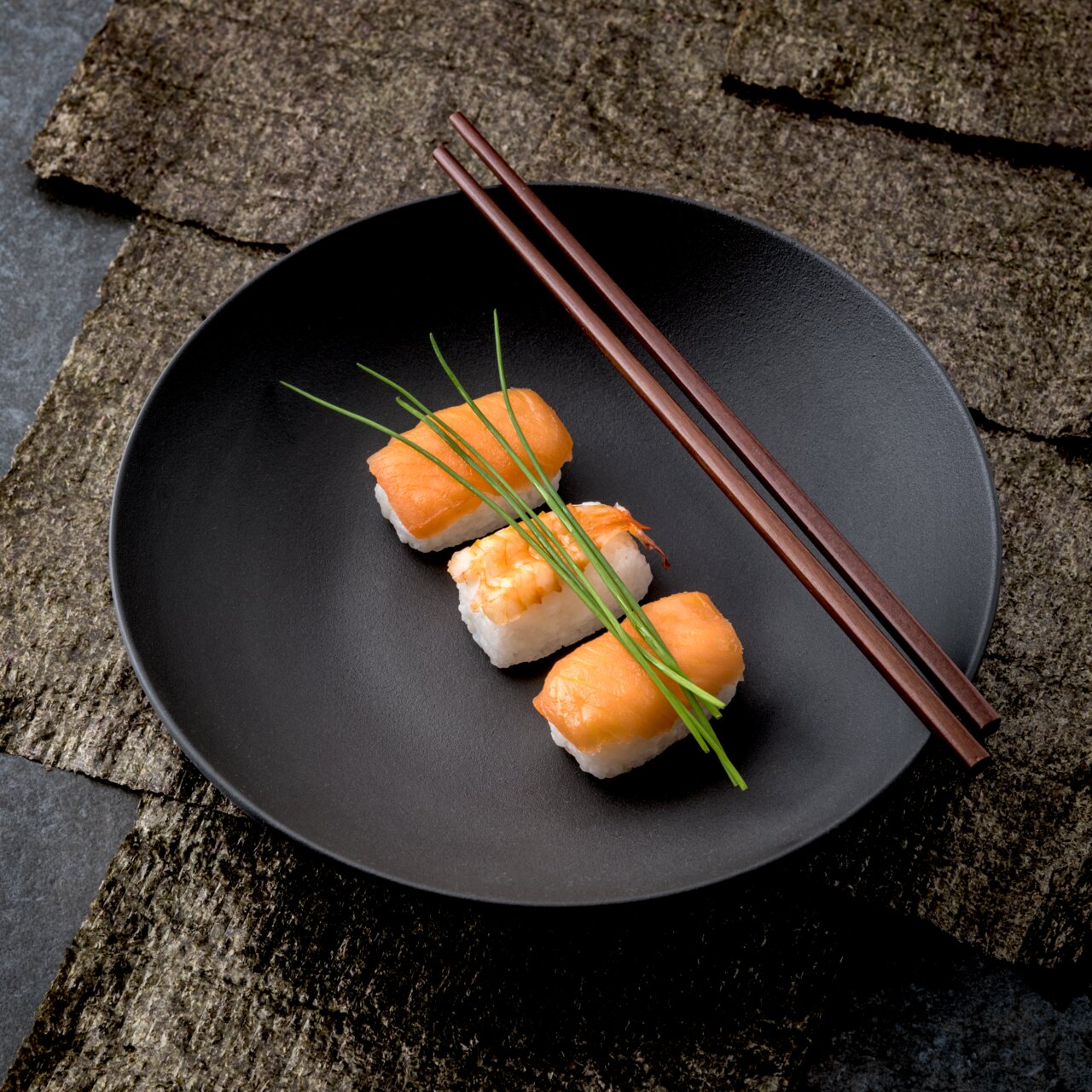 Schwarze Schale mit Sushi und Essstäbchen, von oben fotografiert
