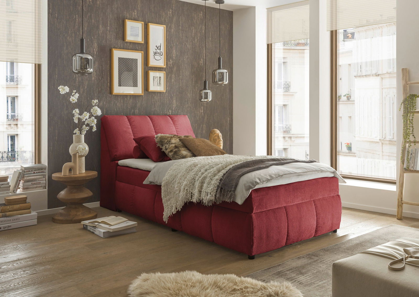 Rotes Boxspringbett in einem stilvoll eingerichteten Schlafzimmer mit Holzboden und großen Fenstern, seitliche Perspektive