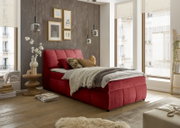 Rood boxspringbed in een stijlvol ingerichte slaapkamer met houten vloer en grote ramen, zijaanzicht