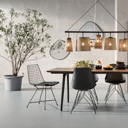 Moderner Essbereich mit einem schwarzen Drahtstuhl im Vordergrund, seitliche Perspektive. Der Raum ist stilvoll mit einem Holztisch, schwarzen Stühlen und hängenden Lampen dekoriert.