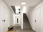 Modernes, helles Treppenhaus mit grauer Betontreppe, weißen Türen und schwarzem Geländer, Deckenleuchte und Pflanze im Obergeschoss; Perspektive: Frontalansicht aus dem Flur in Richtung Treppe.