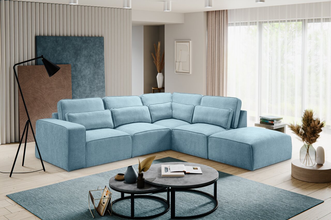 Modernes hellblaues L-förmiges Ecksofa mit breiter Ottomane und vielen Rückenkissen in einem hellen Wohnzimmer, aufgenommen aus frontaler leicht seitlicher Perspektive.