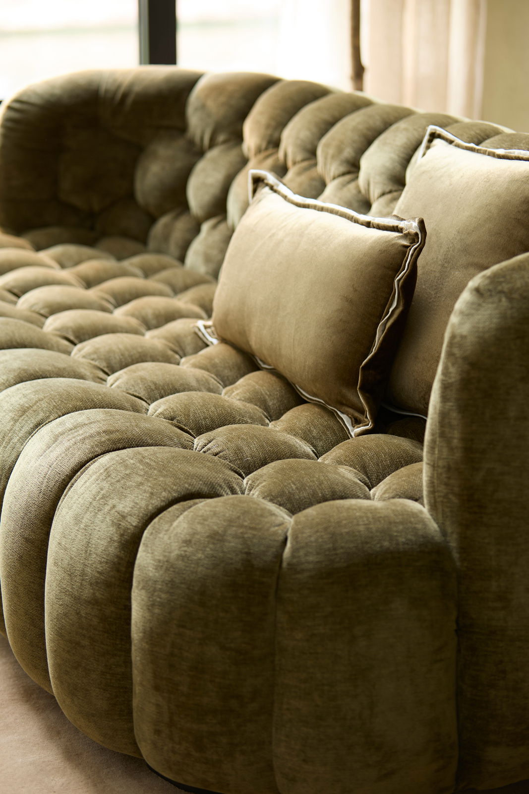 Nahaufnahme einer eleganten, olivgrünen Couch mit weicher Polsterung und dekorativen Kissen, seitliche Perspektive.