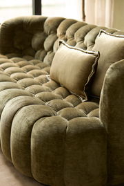 Nahaufnahme einer eleganten, olivgrünen Couch mit weicher Polsterung und dekorativen Kissen, seitliche Perspektive.