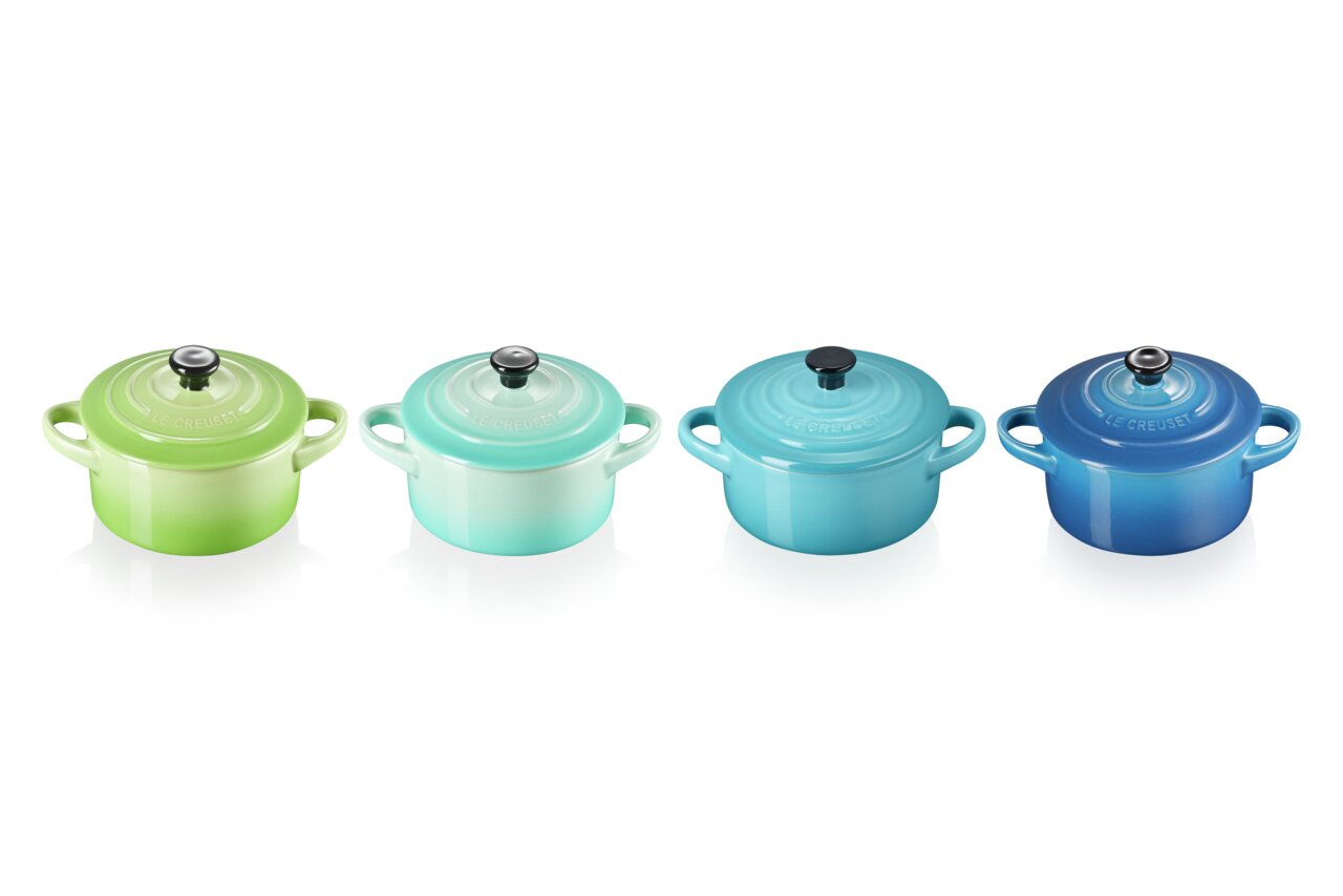 LE CREUSET Mini-Cocotte 4er-Set 10cm MEERESBRIESE Vier Mini-Cocottes in verschiedenen Blautönen und Grün, von oben betrachtet, auf einer reflektierenden Oberfläche.
