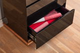 Nahaufnahme eines schwarzen Hochglanz-Sideboards mit geöffneter Schublade, die rote und weiße Stoffe enthält, auf einem Holzboden.