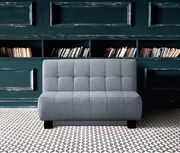 Graues Faltbett in einem stilvollen Raum mit Bücherregal im Hintergrund, Frontalansicht.