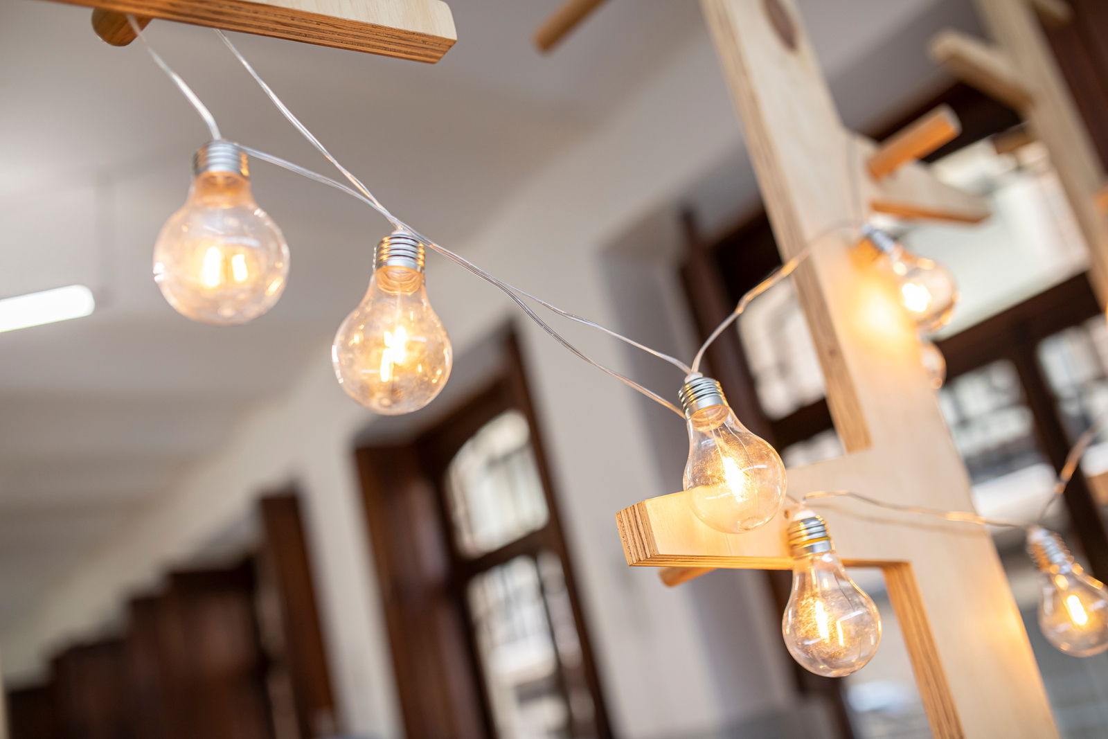 Nahaufnahme einer Girlande mit leuchtenden Glühbirnen, aufgehängt an einem Holzgestell in einem Innenraum.
