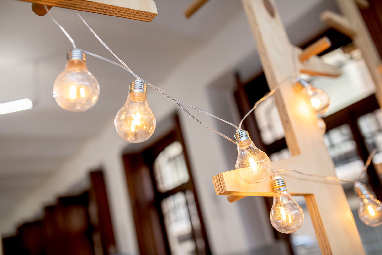 Nahaufnahme einer Girlande mit leuchtenden Glühbirnen, aufgehängt an einem Holzgestell in einem Innenraum.