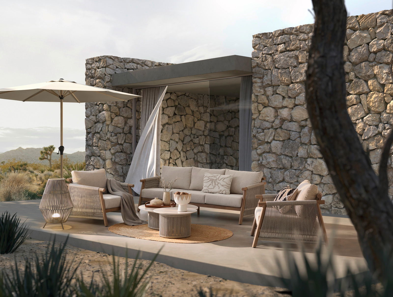 Moderne Loungegarnitur-Set auf einer Terrasse mit Steinmauer im Hintergrund, bestehend aus einem Sofa, zwei Sesseln, einem runden Tisch und einem Sonnenschirm, seitliche Perspektive.