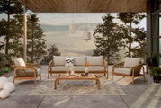 Een loungeset op een terras met uitzicht op een beboste helling bij zonsondergang, bestaande uit een bank, twee fauteuils en een houten salontafel, versierd met kussens en kaarsen.
