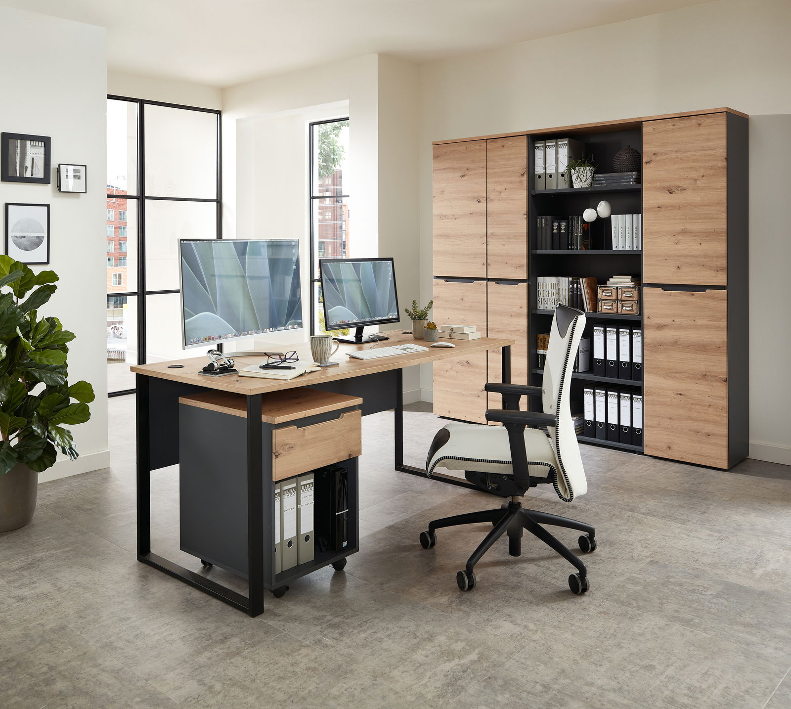 Voleo Schreibtisch DETROIT Moderner Schreibtisch mit Holz- und Metallelementen, ausgestattet mit zwei Monitoren, einem Rollcontainer und einem ergonomischen Bürostuhl, in einem hellen Büro mit Blick auf Aktenschränke im Hintergrund.