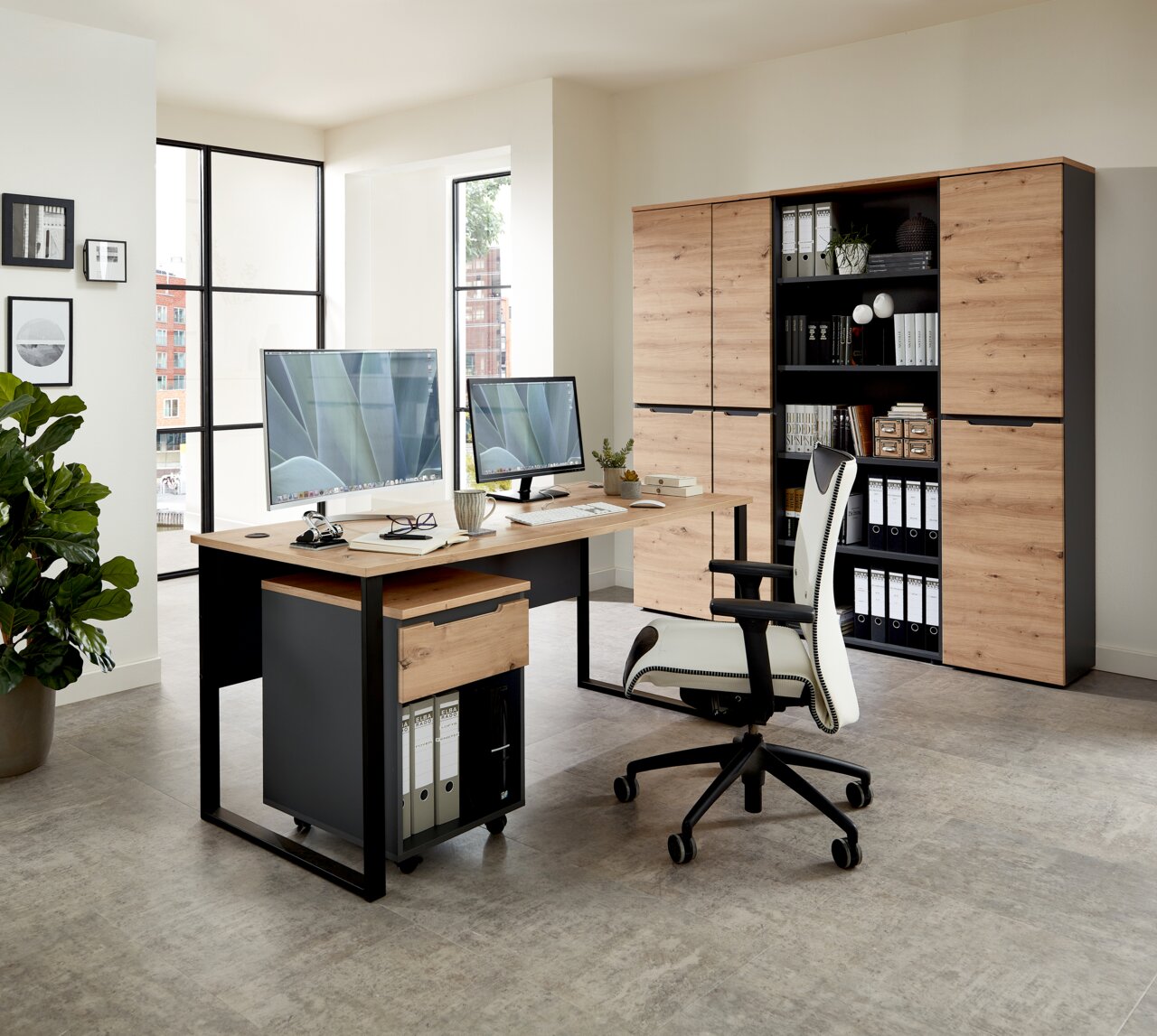 Voleo Schreibtisch DETROIT Moderner Schreibtisch mit Holz- und Metallelementen, ausgestattet mit zwei Monitoren, einem Rollcontainer und einem ergonomischen Bürostuhl, in einem hellen Büro mit Blick auf Aktenschränke im Hintergrund.