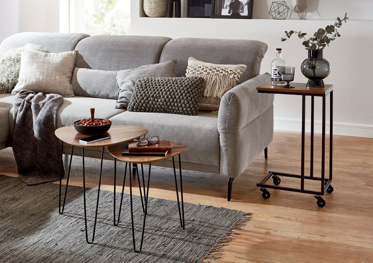 Zurbrüggen Beistelltisch Modernes Wohnzimmer-Setting mit grauem Stoffsofa und Kissen, davor zwei runde Beistelltische mit Holzplatte und schwarzem Metallgestell; rechts ein rollbarer Servierwagen mit Holzplatte und schwarzem Rahmen – Perspektive: frontale, leicht seitliche Ansich