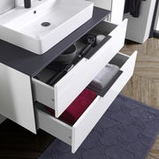 Moderner Waschtisch mit geöffneten Schubladen, gefüllt mit Handtüchern und Pflegeprodukten, aus der Vogelperspektive.