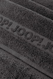 Nahaufnahme eines dunkelgrauen Frottee-Handtuchs mit eingewebtem Schriftzug „TOM TAILOR“, schräg von oben fotografiert.