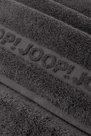 Nahaufnahme eines dunkelgrauen Frottee-Handtuchs mit eingewebtem Schriftzug „TOM TAILOR“, schräg von oben fotografiert.