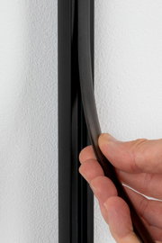 Nahaufnahme einer Hand, die einen schwarzen Sicherheitsabdeckstreifen an einer Wand anbringt.
