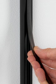 Nahaufnahme einer Hand, die einen schwarzen Sicherheitsabdeckstreifen an einer Wand anbringt.