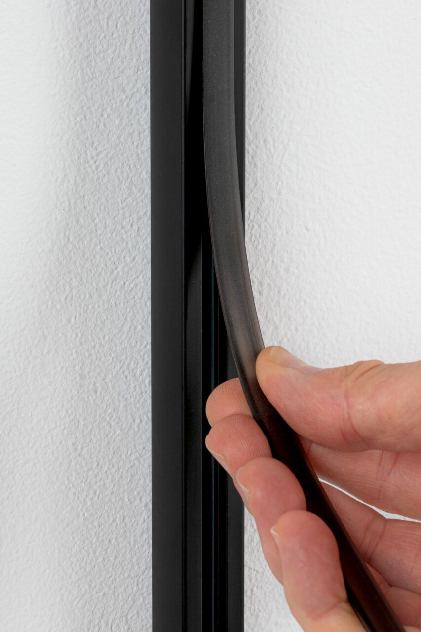 Nahaufnahme einer Hand, die einen schwarzen Sicherheitsabdeckstreifen an einer Wand anbringt.