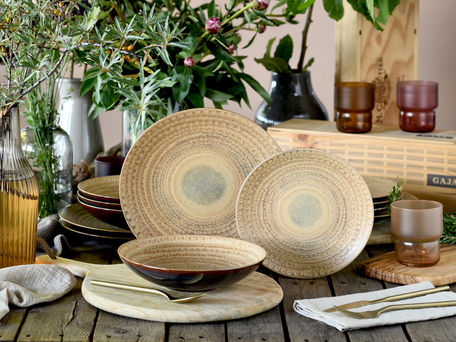 Rustikales Keramik-Geschirrset in Beige mit geprägtem Muster (Teller und Schale) auf Holztisch, dekoriert mit Vasen, Blumen und Besteck; Perspektive: leicht von vorne auf Tischhöhe.