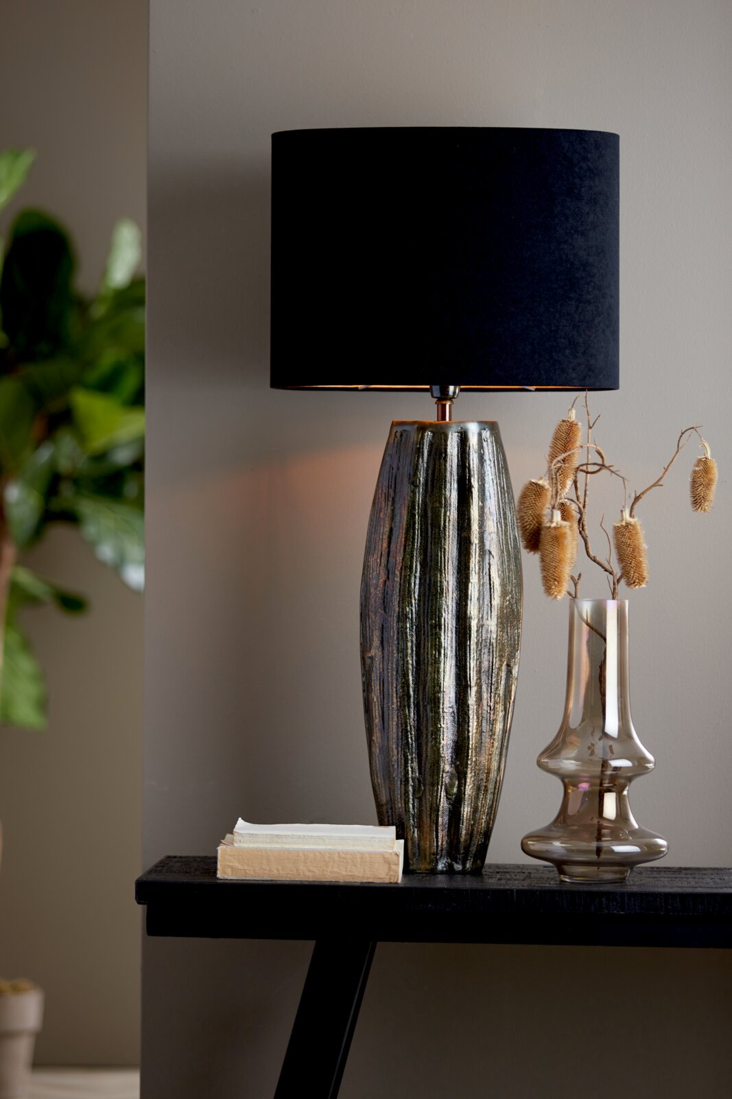 Elegante Tischlampe mit schwarzem, ovalem Lampenschirm und strukturierter, metallisch glänzender Basis, seitliche Perspektive.