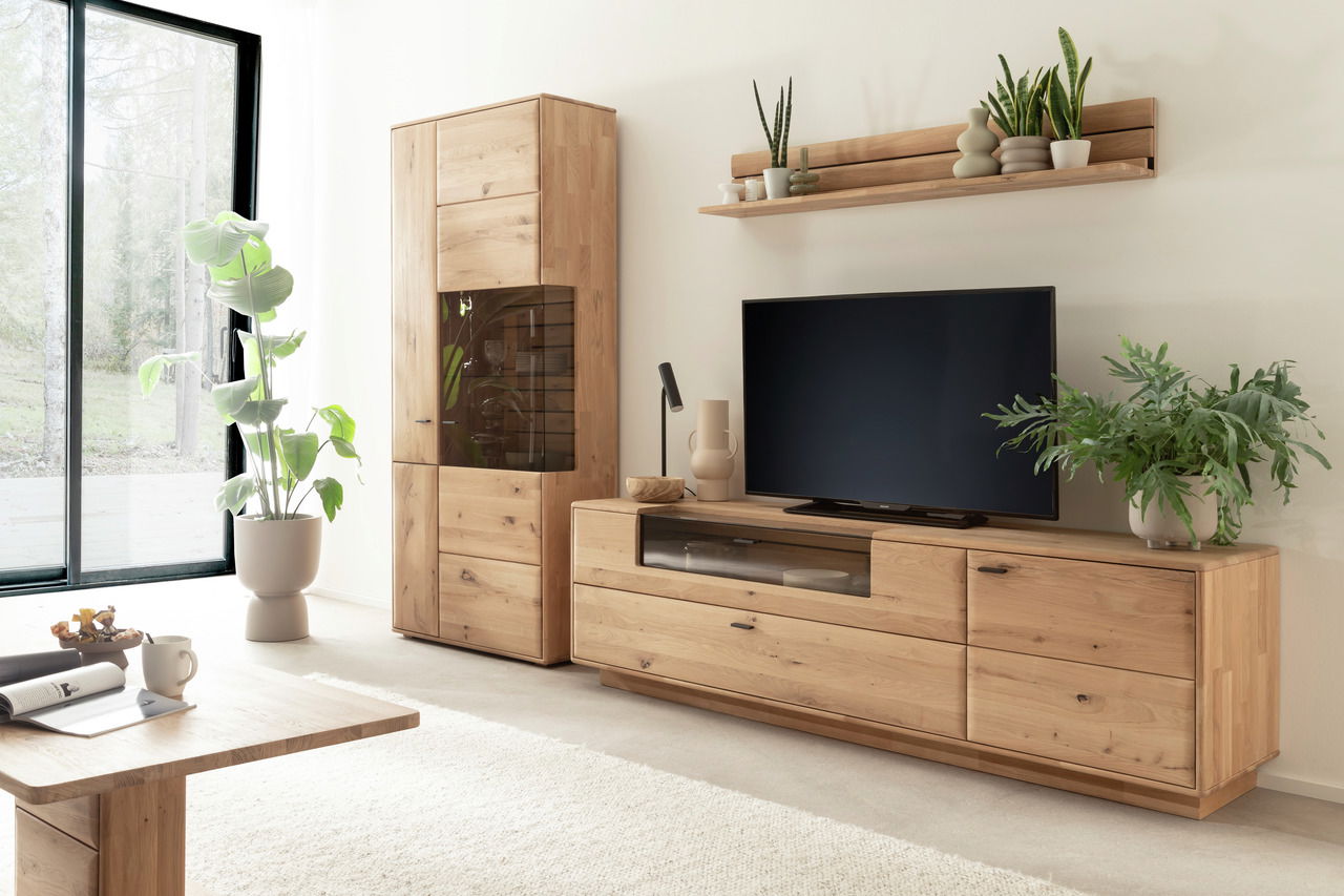 Wohnzimmeransicht mit der Linea Natura Wandkombination GEORGIA aus Holz, bestehend aus einem hohen Schrank, einem TV-Board und einem Wandregal, dekoriert mit Pflanzen und einem Fernseher.