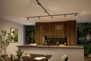 Moderne schwarze LED-Schienenbeleuchtung mit mehreren verstellbaren Spotköpfen an der Decke über einer Küche mit Holzfronten und Kochinsel, Perspektive von schräg unten aus dem Essbereich nach oben