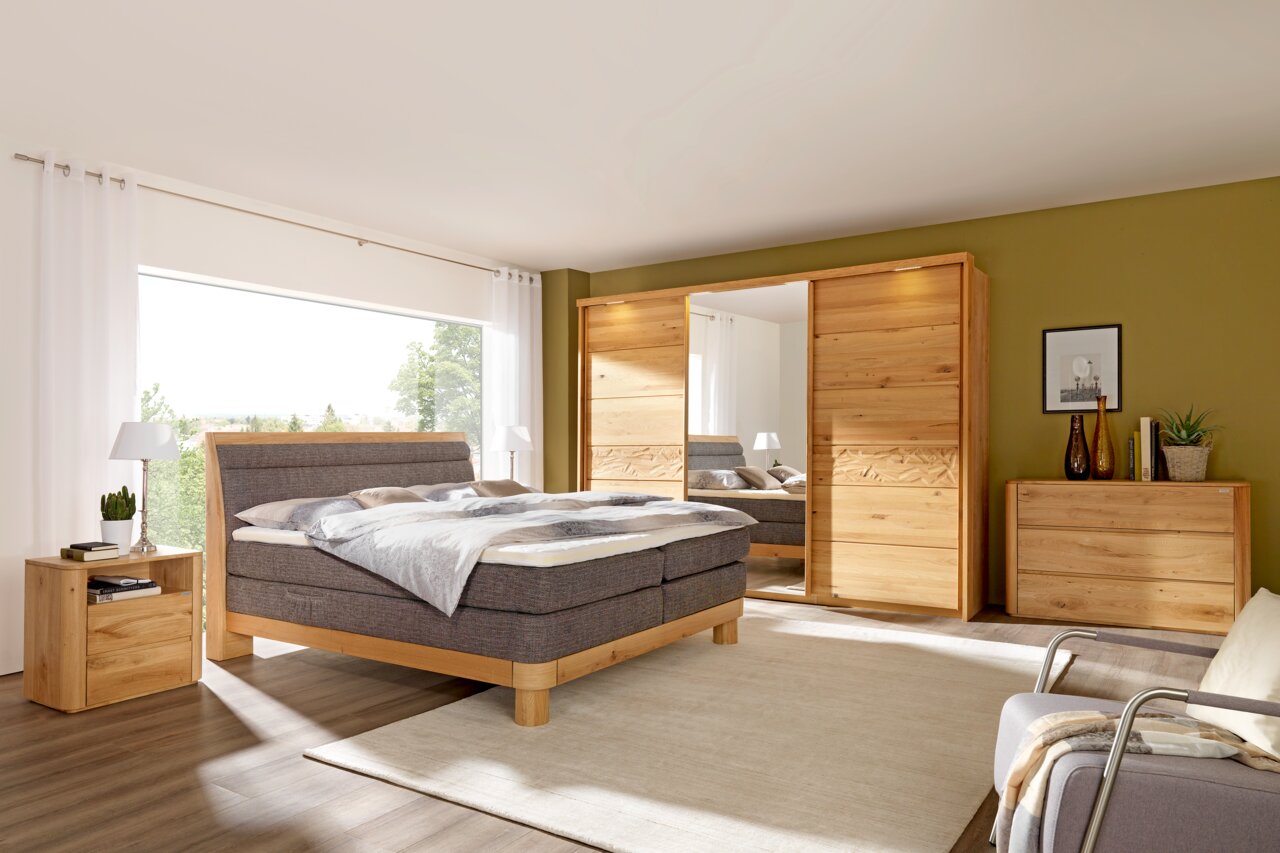 Schlafzimmer mit Schwebetürenschrank aus Holz, Bett und Nachttisch, seitliche Perspektive