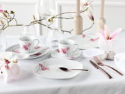 Elegant gedeckter Tisch mit weißem Porzellan-Geschirrset mit rosa Blütenmotiv (Tassen, Teller), Kristallgläsern und roségoldenem Besteck; Ansicht schräg von vorne auf Augenhöhe.