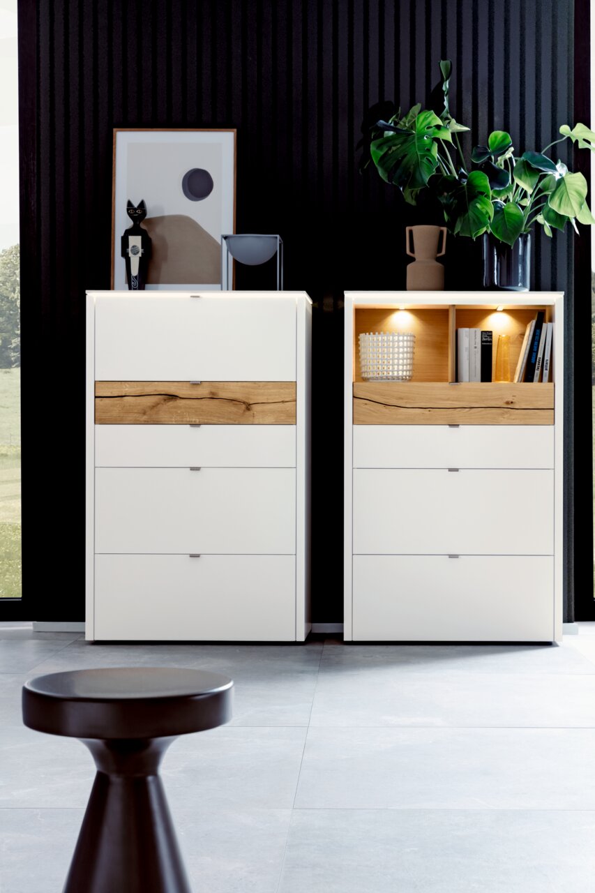 Venjakob Highboard GAME Zwei moderne Highboards in Weiß mit Holzelementen, dekoriert mit Pflanzen und Kunstobjekten, frontal betrachtet.