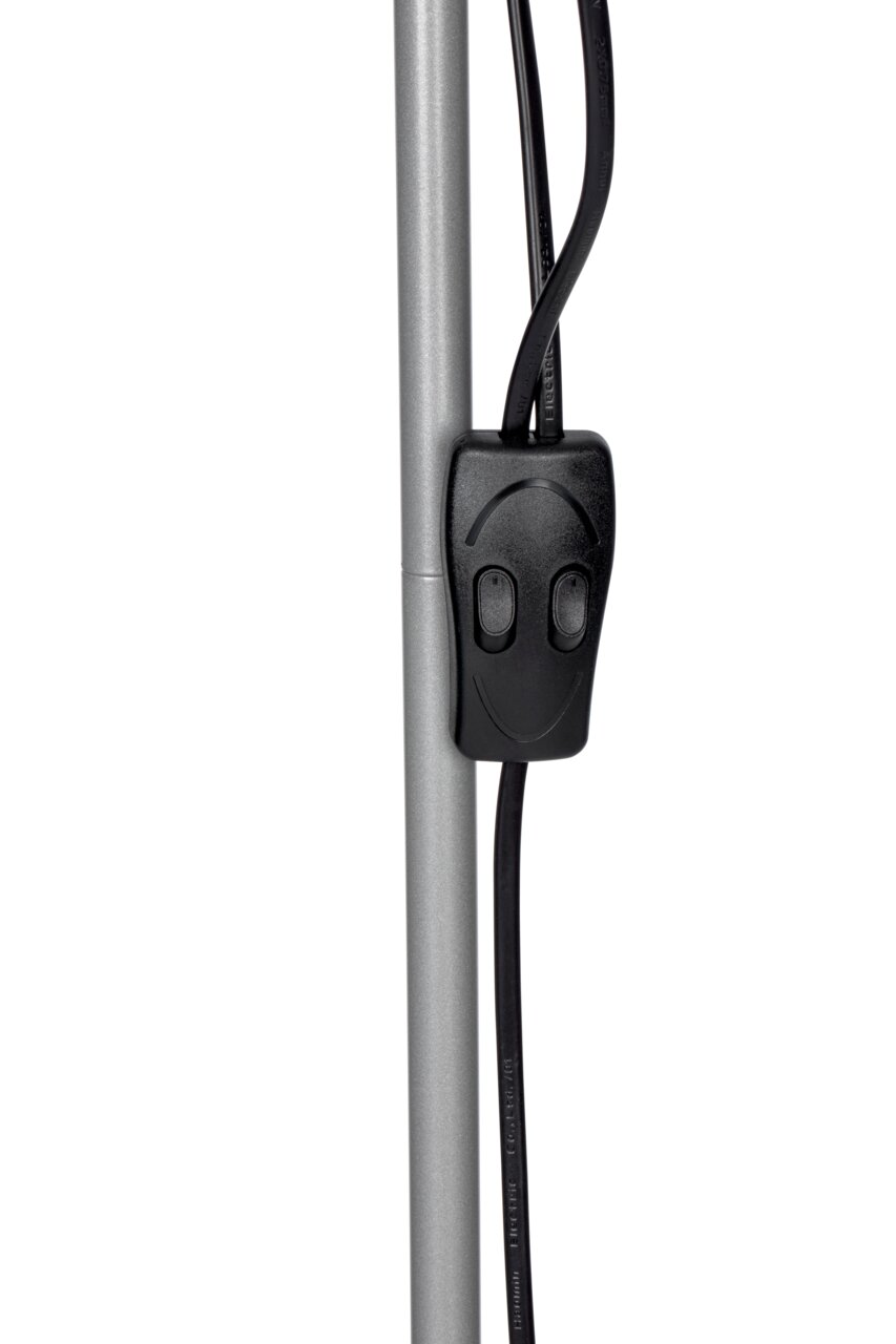 Close-up van een zilveren staande lamp met een zwarte kabel en schakelaar, gezien vanaf de zijkant