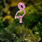 Solarbetriebene Stabbeleuchtung in Form eines rosa Flamingos, seitliche Perspektive, platziert in einem Garten.