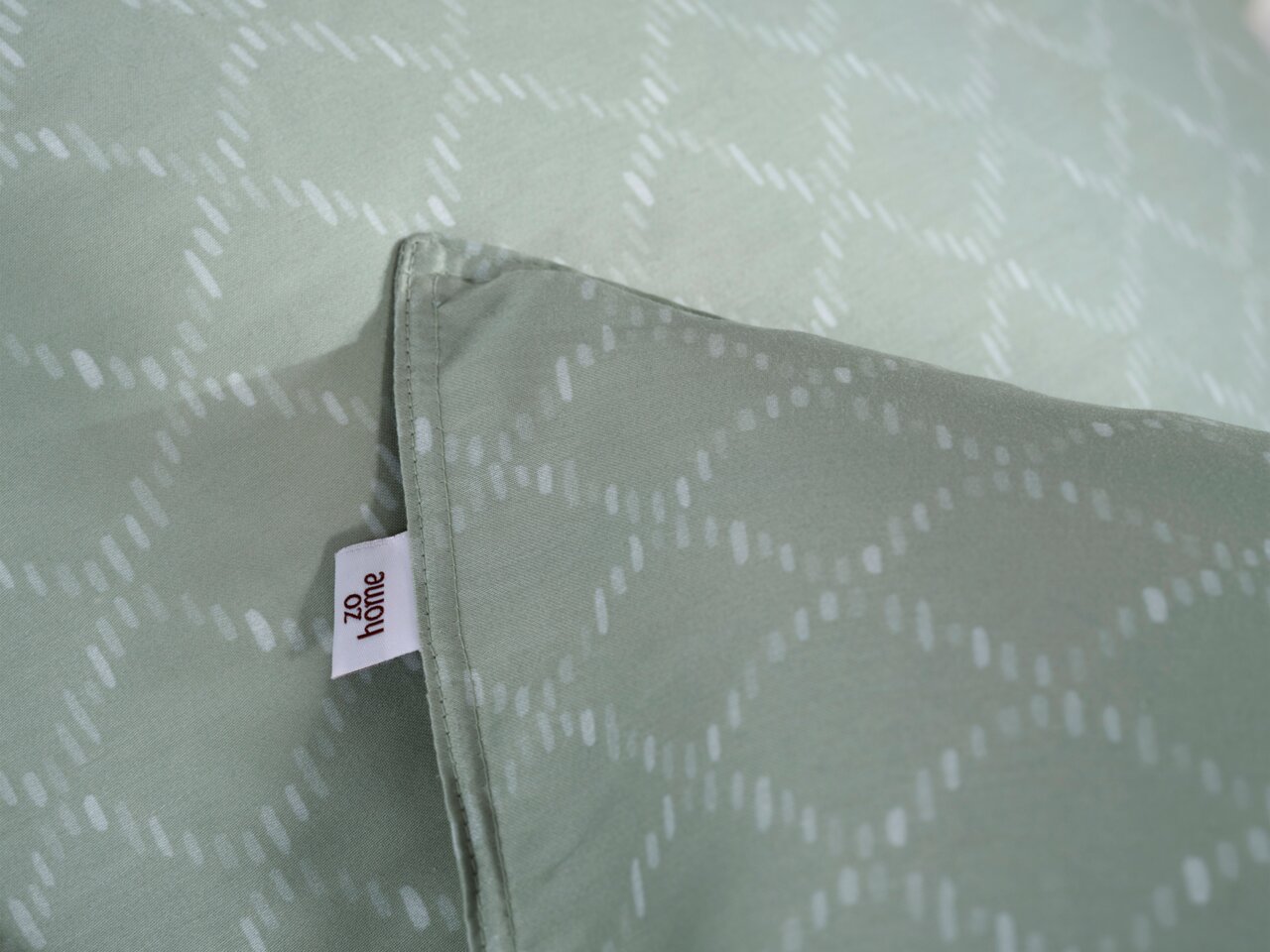 Nahaufnahme einer Bettwäsche in sanftem Grün mit dezentem Muster und einem sichtbaren Etikett.