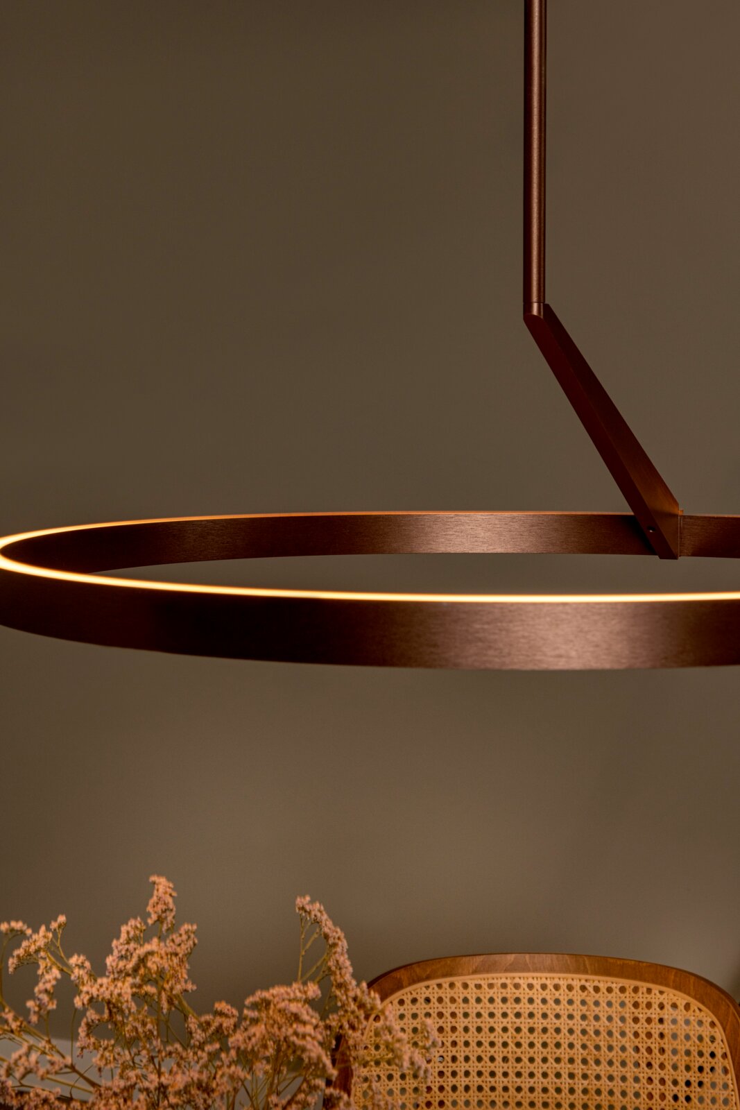 Moderne, ringförmige LED-Pendelleuchte in Bronze/Kupferoptik mit warmweiß leuchtendem Lichtband, schräg von unten im Detail fotografiert