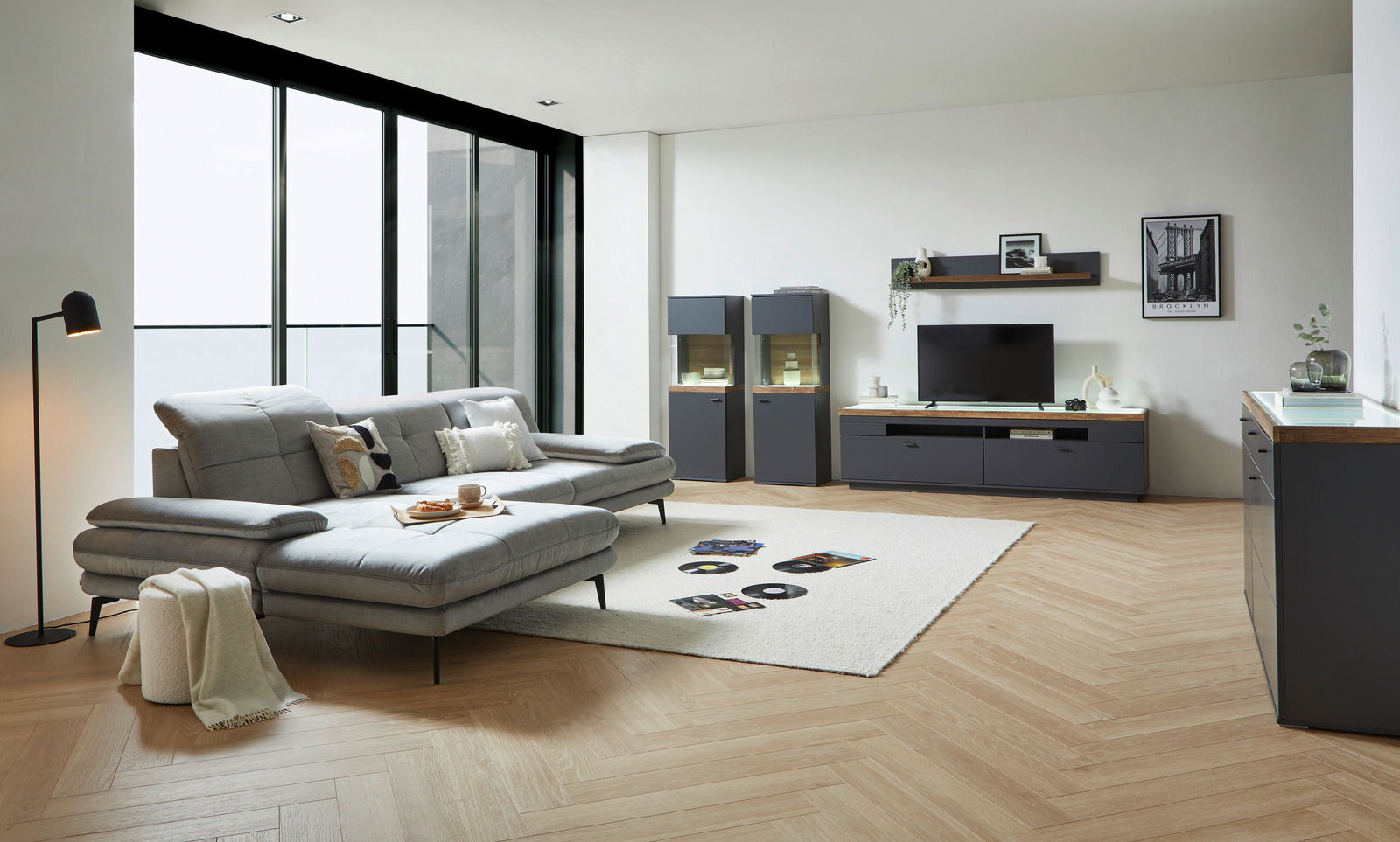 Modernes Wohnzimmer mit grauem Sofa, Couchtisch und TV-Lowboard in einer hellen, stilvollen Umgebung. Perspektive von der Seite.