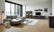 Modernes Wohnzimmer mit grauem Sofa, Couchtisch und TV-Lowboard in einer hellen, stilvollen Umgebung. Perspektive von der Seite.